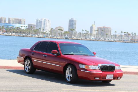 2002 Mercury Grand Marquis - A red 2002 Mercury Grand Marquis is parked near a body of water with a city skyline in the distance.
