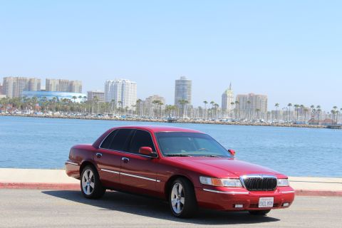 2002 Mercury Grand Marquis - A red 2002 Mercury Grand Marquis is parked near a waterfront with a city skyline visible.