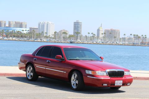 2002 Mercury Grand Marquis - Red 2002 Mercury Grand Marquis parked near a harbor with a city skyline behind it.