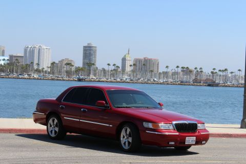 2002 Mercury Grand Marquis - A red 2002 Mercury Grand Marquis is parked near a harbor with a city skyline.