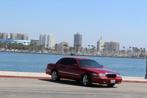 2002 Mercury Grand Marquis - A red 2002 Mercury Grand Marquis is parked near a waterfront with a city skyline in the distance.