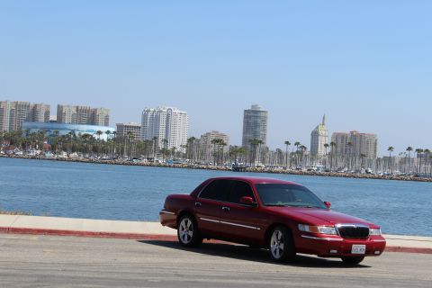 2002 Mercury Grand Marquis - A red 2002 Mercury Grand Marquis is parked near a body of water with a city skyline in the distance.
