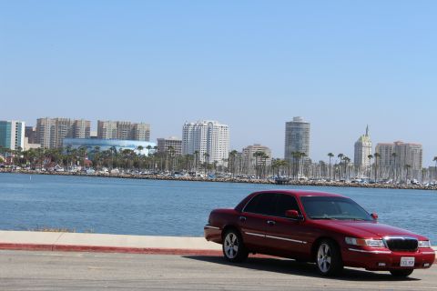 2002 Mercury Grand Marquis - A red 2002 Mercury Grand Marquis is parked near a waterfront with a city skyline.