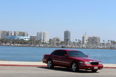 2002 Mercury Grand Marquis - A red 2002 Mercury Grand Marquis is parked near a waterfront with a city skyline visible.