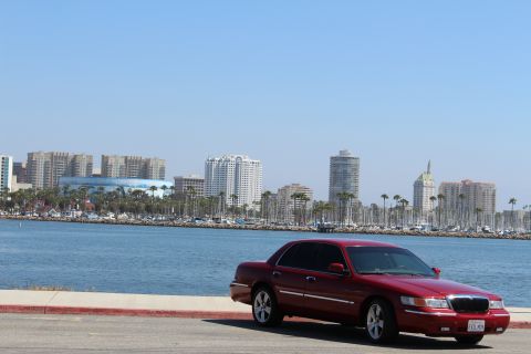 2002 Mercury Grand Marquis - A red 2002 Mercury Grand Marquis is parked near a body of water with a city skyline visible in the distance.