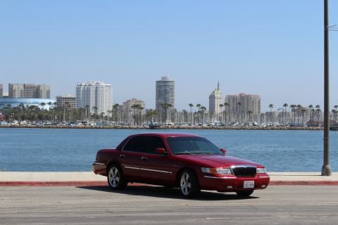 2002 Mercury Grand Marquis - A red 2002 Mercury Grand Marquis is parked near a body of water with a city skyline in the background.