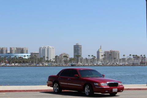 2002 Mercury Grand Marquis - A red 2002 Mercury Grand Marquis is parked near a waterfront with a city skyline and palm trees.