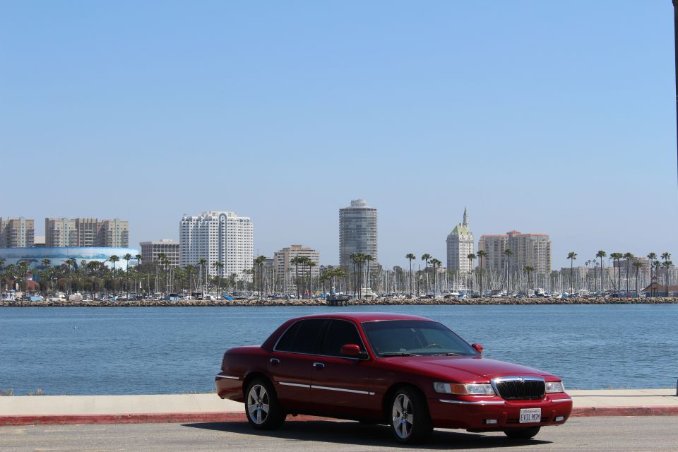 Red 2002 Mercury Grand Marquis parked by the water with a city skyline in the background