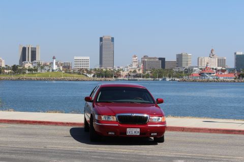 2002 Mercury Grand Marquis - A red 2002 Mercury Grand Marquis is parked in front of a city skyline and a body of water.