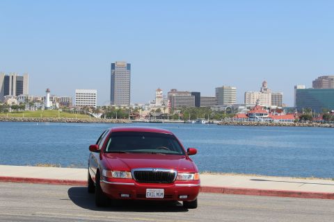 2002 Mercury Grand Marquis - A red 2002 Mercury Grand Marquis is parked near a body of water with a city skyline visible.