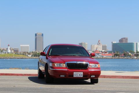 2002 Mercury Grand Marquis - A red 2002 Mercury Grand Marquis is parked in front of a city skyline and a body of water.
