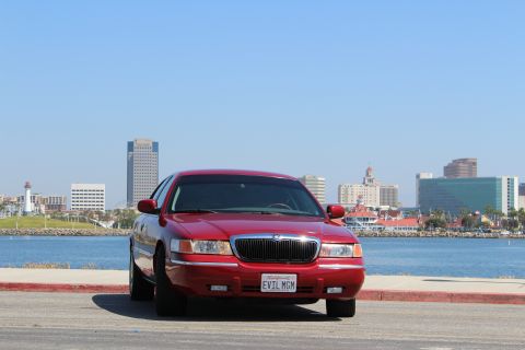 2002 Mercury Grand Marquis - A red 2002 Mercury Grand Marquis is parked with a waterfront city view.