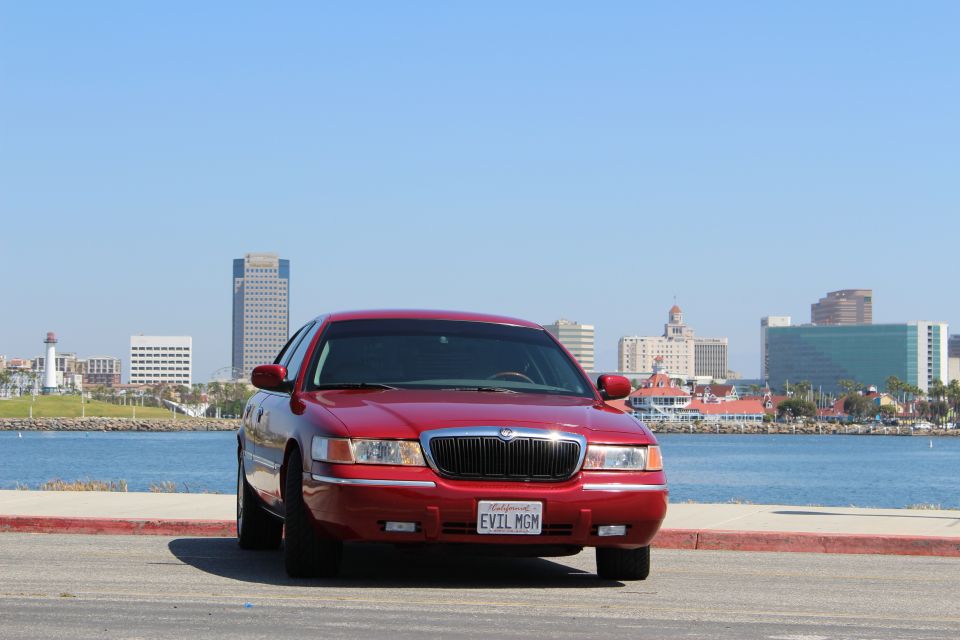 Red 2002 Mercury Grand Marquis parked by the water with a city skyline in the background