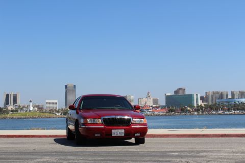 2002 Mercury Grand Marquis - A red 2002 Mercury Grand Marquis is parked facing forward with a city skyline and water behind it.