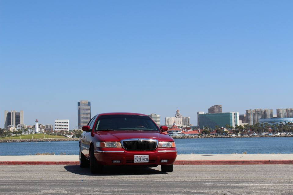 Red 2002 Mercury Grand Marquis parked by the water, front view, with a city skyline in the background