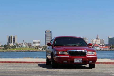 2002 Mercury Grand Marquis - Red Mercury Grand Marquis sedan parked with a city skyline and water in the background.