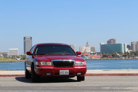 2002 Mercury Grand Marquis - A red Mercury Grand Marquis is parked by the water with a city skyline in the distance.