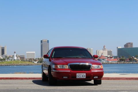 2002 Mercury Grand Marquis - A red 2002 Mercury Grand Marquis is parked facing the camera with a city skyline and water in the background.