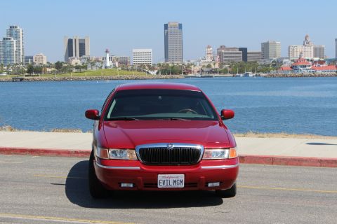 2002 Mercury Grand Marquis - A red 2002 Mercury Grand Marquis is seen from the front with a city skyline in the background.