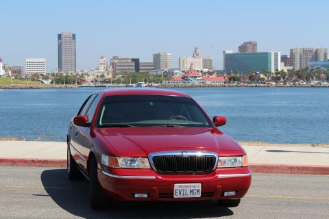 2002 Mercury Grand Marquis - Front view of a red 2002 Mercury Grand Marquis sedan with a custom license plate, parked near a waterfront city.