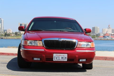 2002 Mercury Grand Marquis - A red 2002 Mercury Grand Marquis is seen from the front with a waterfront cityscape in the background.