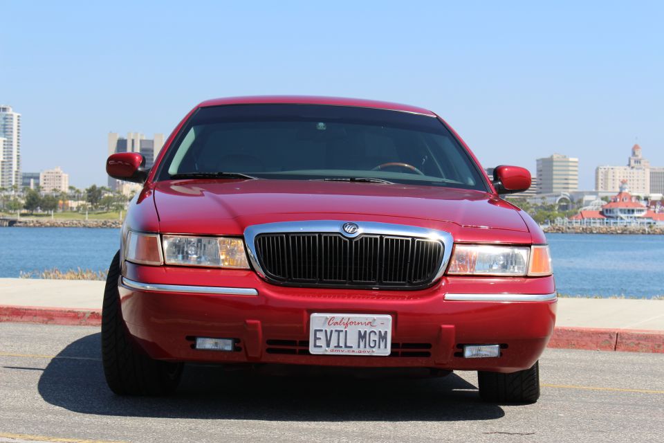 Red 2002 Mercury Grand Marquis with custom license plate 'EVIL MGM' parked by the water