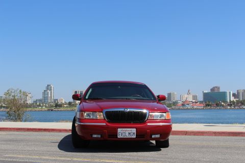 2002 Mercury Grand Marquis - Front view of a red 2002 Mercury Grand Marquis with a city skyline and water in the background.