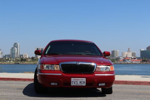 2002 Mercury Grand Marquis - A red Mercury Grand Marquis is parked by the water with a city skyline in the distance.