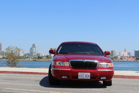 2002 Mercury Grand Marquis - A red 2002 Mercury Grand Marquis is parked by the water with a city skyline in the background.