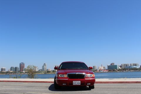 2002 Mercury Grand Marquis - A red 2002 Mercury Grand Marquis is seen from the front with a city skyline in the background.