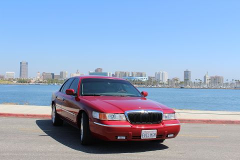 2002 Mercury Grand Marquis - A red 2002 Mercury Grand Marquis is parked by the water with a city skyline.