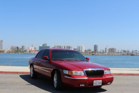 2002 Mercury Grand Marquis - A red 2002 Mercury Grand Marquis is parked near a body of water with a city skyline visible.