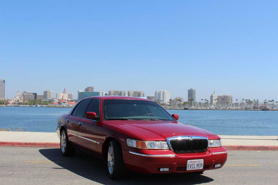 Red 2002 Mercury Grand Marquis parked by the water with a city skyline in the background