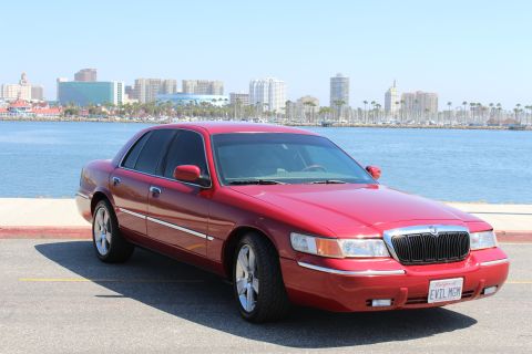 2002 Mercury Grand Marquis - A red 2002 Mercury Grand Marquis is parked near the water with a city skyline.