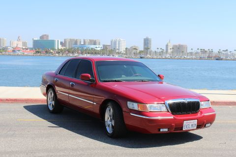 2002 Mercury Grand Marquis - A red 2002 Mercury Grand Marquis is parked near a waterfront with a city skyline visible.