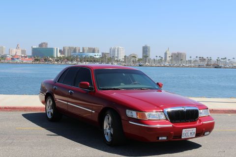 2002 Mercury Grand Marquis - A red 2002 Mercury Grand Marquis is parked by the water, with a city skyline visible in the distance.