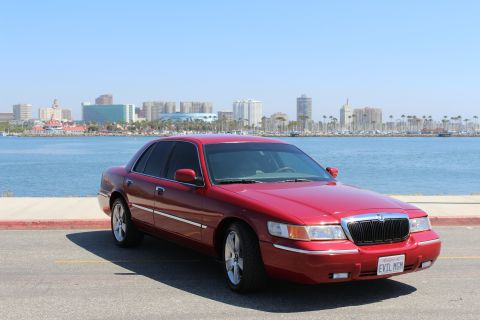 2002 Mercury Grand Marquis - A red 2002 Mercury Grand Marquis is parked near a body of water with a city skyline visible.