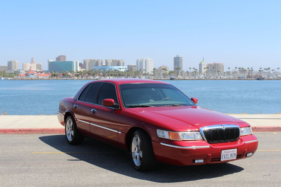 Red 2002 Mercury Grand Marquis parked by a waterfront with a city skyline in the background