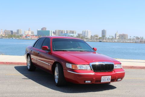2002 Mercury Grand Marquis - A red 2002 Mercury Grand Marquis is parked near a waterfront with a city skyline visible in the distance.