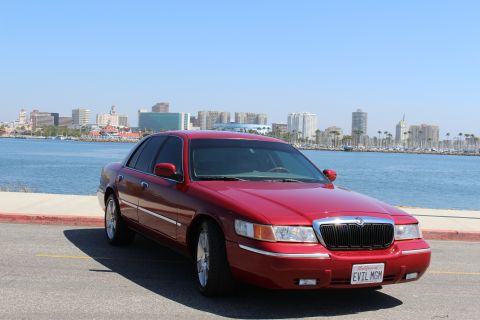 2002 Mercury Grand Marquis - A red 2002 Mercury Grand Marquis is parked near a body of water, with a city skyline visible across the water.