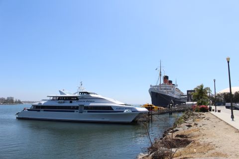 2002 Mercury Grand Marquis - Two large ships, a modern ferry and the historic Queen Mary, are docked side-by-side in a sunny harbor.