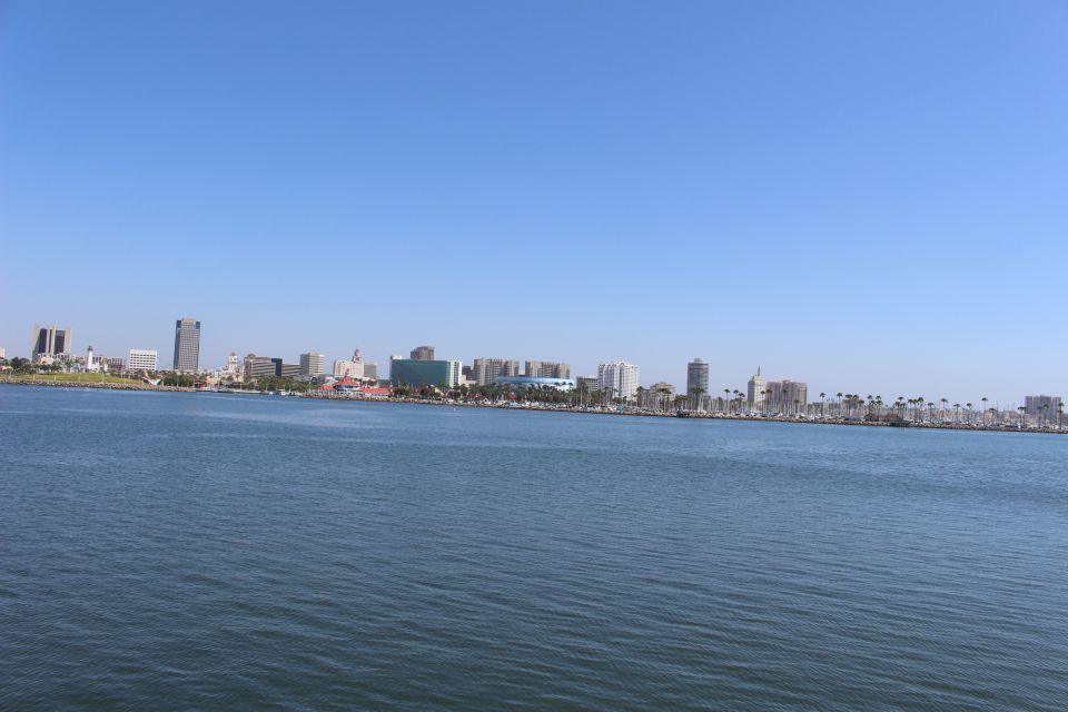 City skyline with buildings and palm trees visible across a wide expanse of blue water under a clear sky. Watermark reads SUPERMOTORS