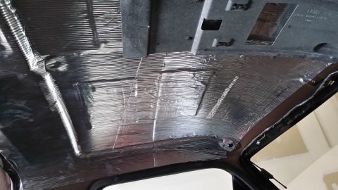 1994 Ford Bronco - The interior ceiling of a vehicle is covered with soundproofing material, revealing exposed metal and wiring underneath.