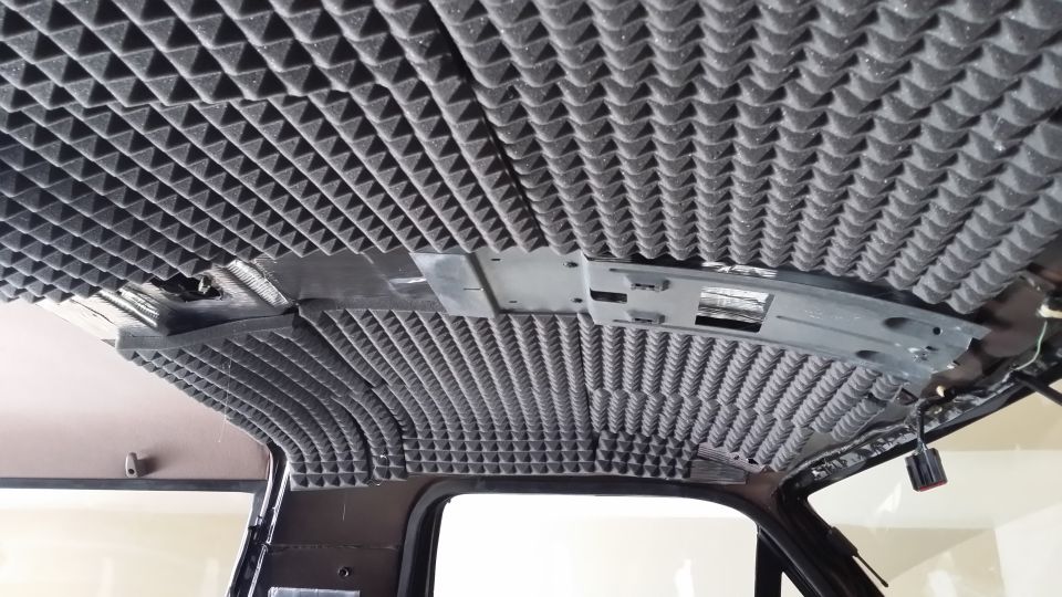 Vehicle interior ceiling covered in pyramid-shaped soundproofing foam, with exposed wiring and mounting brackets