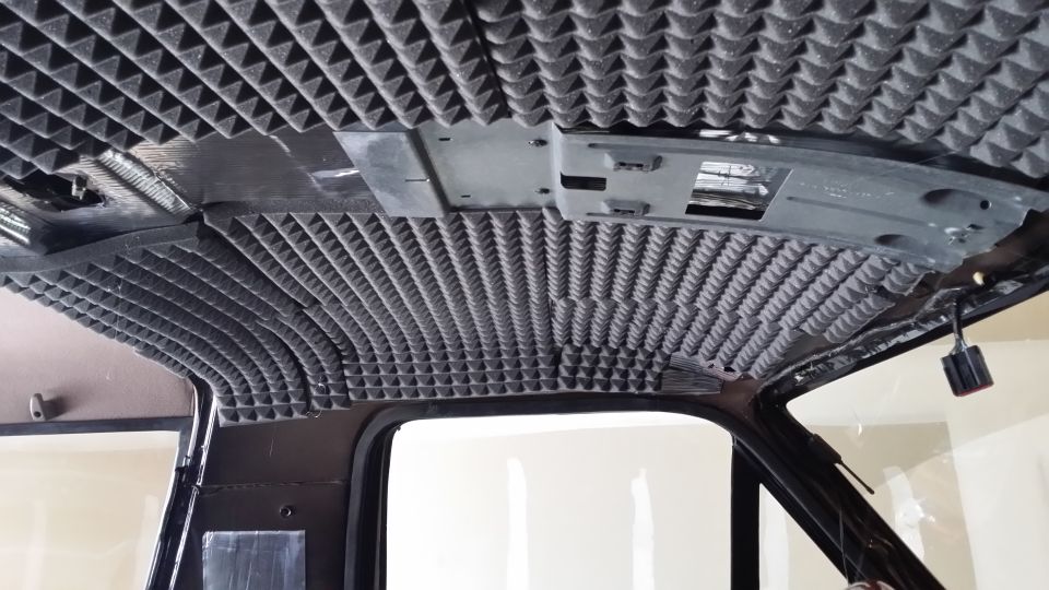 Vehicle ceiling covered in pyramid-shaped soundproofing foam, showing exposed metal structure and wiring
