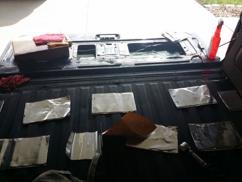 1994 Ford Bronco - Soundproofing material is being applied to the bed of a pickup truck, with tools and a red bottle visible.