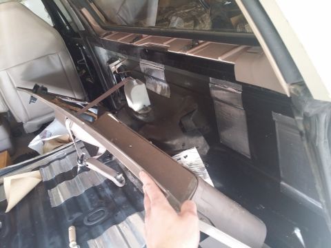1994 Ford Bronco - Soundproofing is being applied to the rear interior panels of a vehicle, with a trim piece held by a hand.