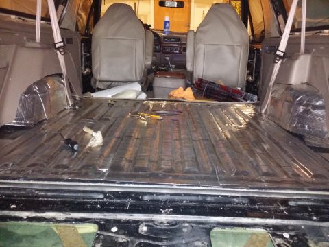 1994 Ford Bronco - The rear cargo area of an SUV is being prepared for soundproofing, with insulation applied to the floor and wheel wells.