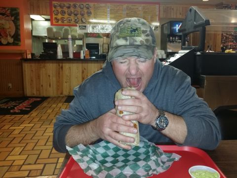 1994 Ford Bronco - A man aggressively eats a large burrito while sitting at a table in a restaurant.