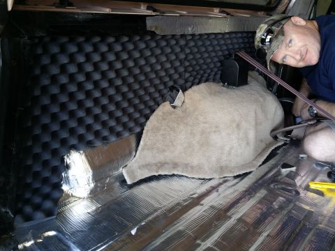 1994 Ford Bronco - A person is installing soundproofing material in the cargo area of a vehicle.